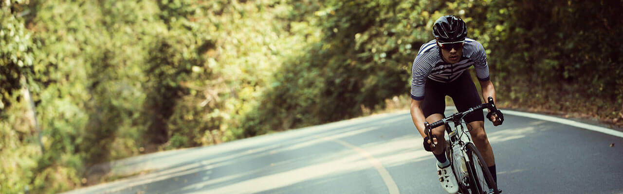 A man on a road bike wearing a helmet, cycling shoes and sunglasses riding on a road.