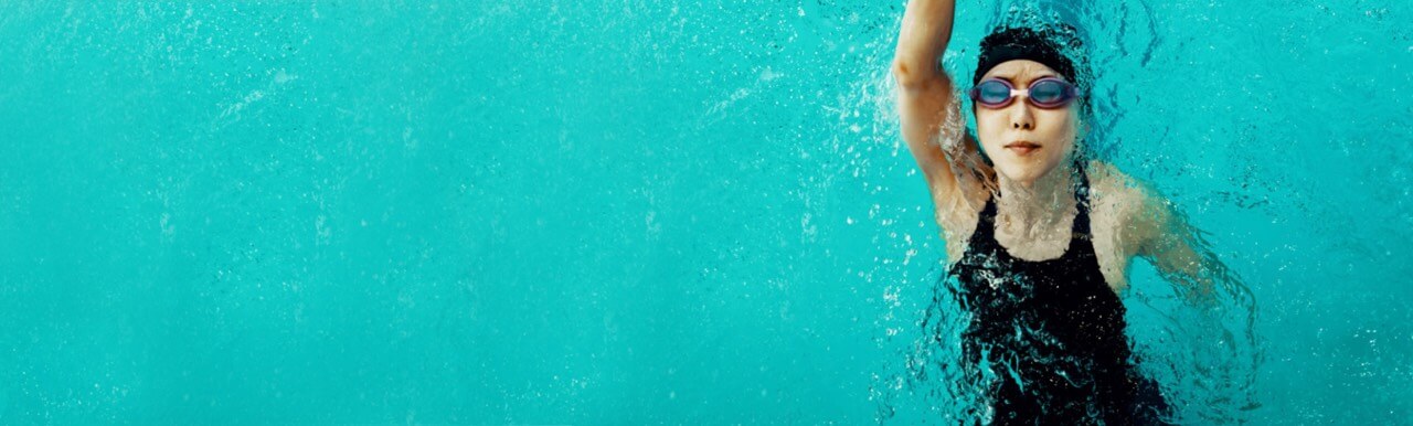 Woman swimming in a swimming pool with goggles and a swimming hat on