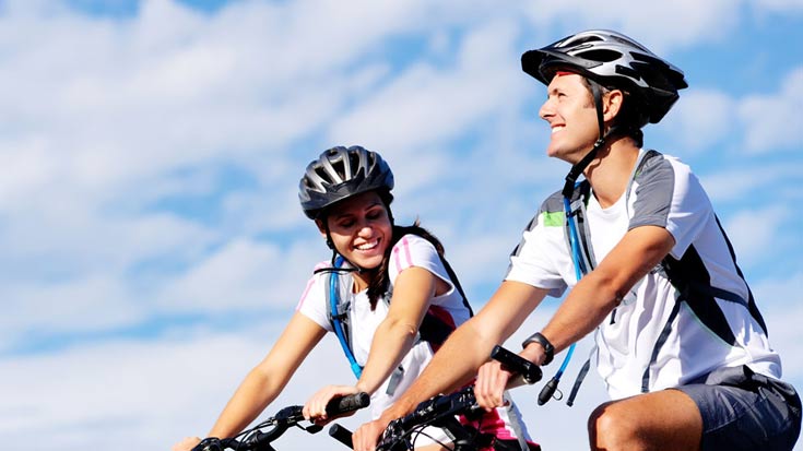 Two people smiling as they ride their bikes together on a sunny day.